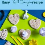 A colorful flat lay of heart-shaped and flower-shaped salt dough ornaments on a green mat, surrounded by plastic cookie cutters and modeling tools—perfect for a rainy day. Text reads: Easy Salt Dough recipe. unicornsdinosaursandme.com.