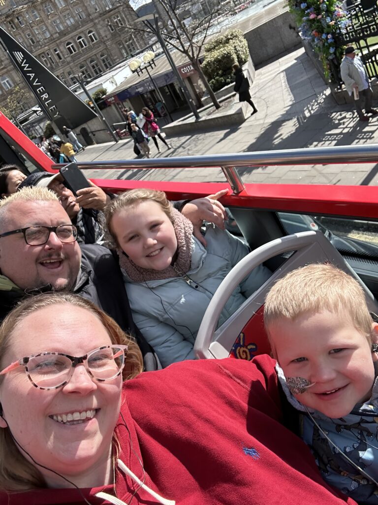 A Family of Four On An Open Top Bus Tour In Edinburgh Outside Waverley Train Station